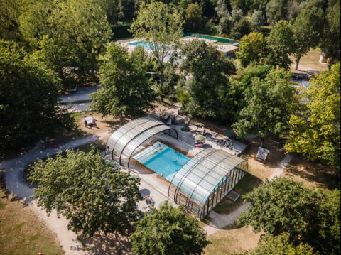 Vista aérea de una piscina cubierta rodeada de vegetación en Huttopia Les Châteaux, en el centro de Francia.