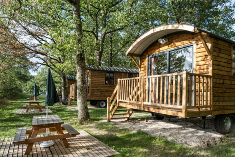 Pequeñas cabañas de madera y mesas de picnic entre árboles en Huttopia Les Châteaux, Centre-Val de Loire, Francia.