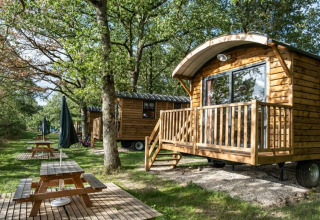 Små træhytter og picnicborde blandt grønne træer på Huttopia Les Châteaux i Centre-Val de Loire, Frankrig.