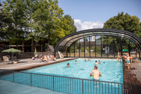 Piscina al aire libre con personas nadando y relajándose, rodeada de árboles en Huttopia Les Châteaux.