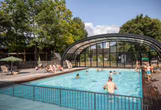 Udendørs swimmingpool med folk, der svømmer og slapper af, omgivet af træer i Huttopia Les Châteaux.