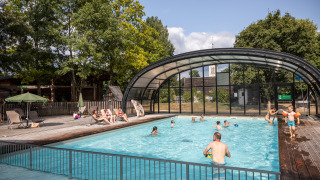 Piscina al aire libre con personas nadando y relajándose, rodeada de árboles en Huttopia Les Châteaux.