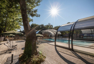 Solrigt udendørs poolområde med træterrasse og overdækning på Huttopia Les Châteaux i Centre-Val de Loire.