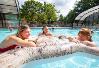 Tre kvinder slapper af på en oppustelig luftmadras i poolen på Huttopia Les Châteaux i Centre-Val de Loire.