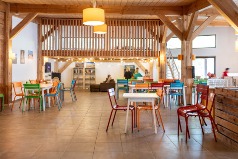 Espacio comunitario en Huttopia Les Châteaux con sillas de colores, vigas de madera y ambiente acogedor.