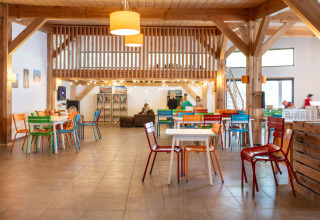 Gemeinschaftsraum im Huttopia Les Châteaux mit bunten Stühlen, Holzbalken und geselligem Ambiente.