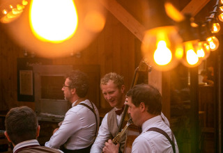 Musikere spiller under hyggelige lyskæder på en restaurant i Huttopia Les Châteaux, Centre-Val de Loire, Frankrig.
