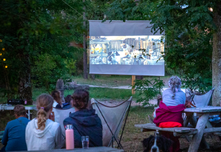 Udendørs biografvisning om aftenen i skoven med familier og hund ved Huttopia Les Châteaux, Frankrig.
