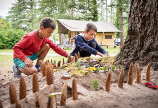 Deux garçons jouent avec des voitures miniatures et des pommes de pin au parc Huttopia Les Châteaux.