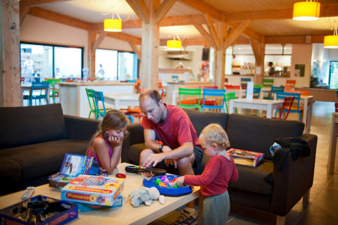 Familia juega juegos de mesa en la sala común del parque vacacional Huttopia Les Châteaux en Francia.