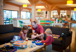 Familie leger brætspil sammen i en moderne opholdsstue på ferieparken Huttopia Les Châteaux, Frankrig.