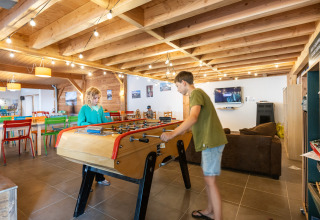 To børn spiller bordfodbold i et lyst, træbeklædt opholdsrum på Huttopia Les Châteaux, Frankrig.