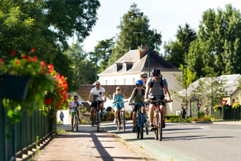Familien fahren mit Fahrrädern auf einer sonnigen Straße im Ferienpark Huttopia Les Châteaux, Centre-Val de Loire.