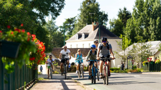 Familias paseando en bicicleta bajo el sol en Huttopia Les Châteaux, un parque vacacional en Centre-Val de Loire.