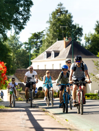 Familias paseando en bicicleta bajo el sol en Huttopia Les Châteaux, un parque vacacional en Centre-Val de Loire.