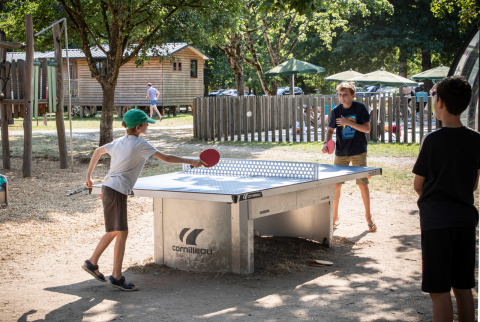 Niños juegan al ping-pong al aire libre en Huttopia Les Châteaux, parque vacacional en Centre-Val de Loire, Francia.