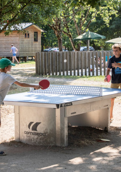 Niños juegan al ping-pong al aire libre en Huttopia Les Châteaux, parque vacacional en Centre-Val de Loire, Francia.