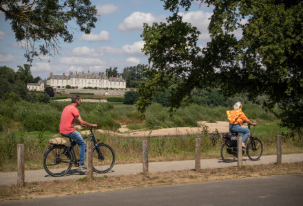 Dos personas montan en bicicleta por un sendero con un gran castillo de fondo cerca de Bracieux, Centro-Valle de Loira, Francia.