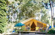 Familia relajándose frente a una tienda safari Bungalow Classic en Huttopia Oléron Les Chênes Verts, rodeada de bosque.