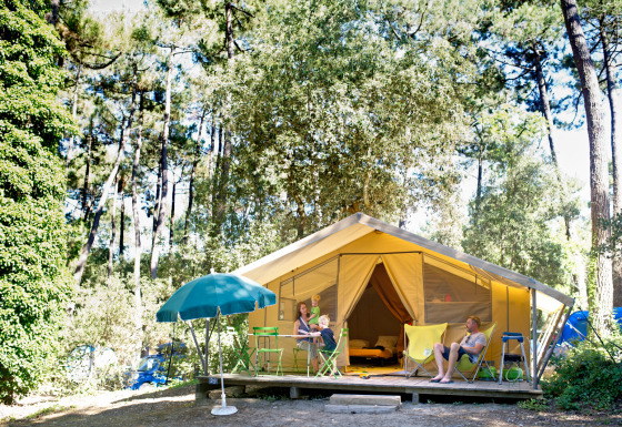 Familie entspannt vor einem Safari-Bungalowzelt Classic bei Huttopia Oléron Les Chênes Verts im Wald in Frankreich.