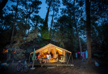 Lit-up Bungalow tent Classic safari tent in the woods at dusk, people dining at a table outside.
