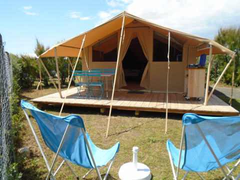 Safari Bungalow Classic-Zelt mit Holzterrasse, blauen Gartenmöbeln und gemütlichen Stühlen draußen.