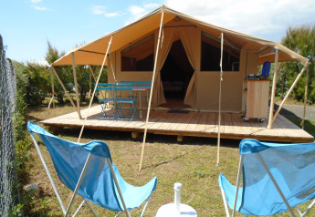Tenda safari Bungalow Classic con veranda in legno, arredi blu da esterno e sedie relax nel giardino.