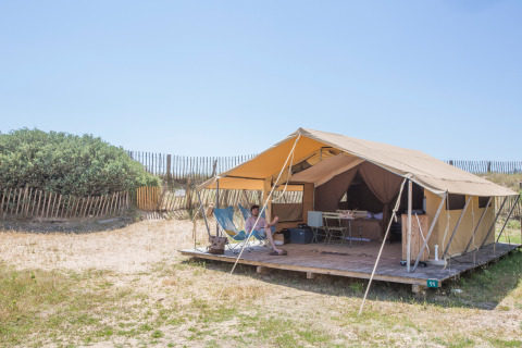 Tenda bungalow Classic a Huttopia Côte Sauvage, Francia, con terrazza, persona e scenario naturale.