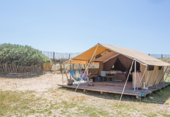 Safari tent Bungalow Classic at Huttopia Côte Sauvage, France, featuring a deck, person, and rustic landscape.