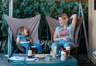 Mor og datter griner sammen i en safari bungalowtelt ved Huttopia Côte Sauvage, Frankrig, under et solsejl.