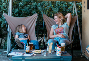 Mother and daughter laughing and relaxing in a safari tent at Huttopia Côte Sauvage, France, under a canopy.