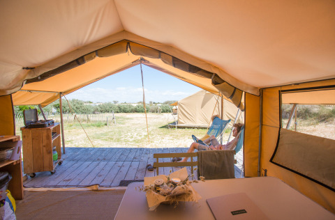 Uitzicht vanuit een safaritent-bungalow bij Huttopia Côte Sauvage, persoon ontspant buiten.