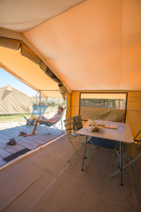 Interior de una tienda safari Bungalow Classic en Huttopia Côte Sauvage, Francia, con una persona relajándose.