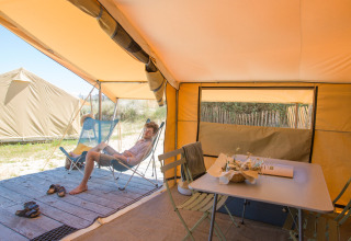 Interior de una tienda safari Bungalow Classic en Huttopia Côte Sauvage, Francia, con una persona relajándose.