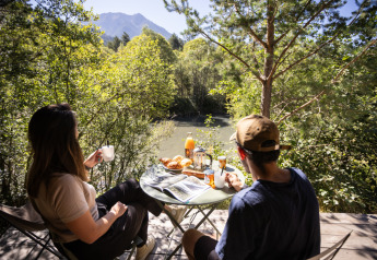 Dos personas disfrutan de un desayuno al aire libre con vistas al río y las montañas en Huttopia la Clarée, Francia.