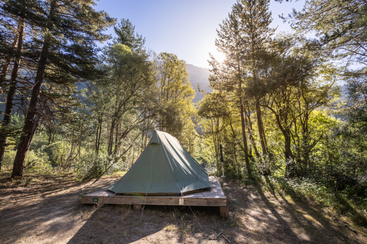 La tienda tipi Bonaventure sobre una plataforma de madera en un bosque soleado en Huttopia la Clarée, Francia.