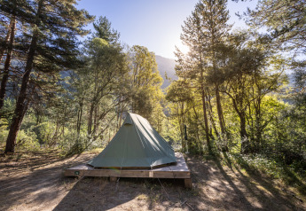 The Bonaventure teepee tent on a wooden platform in a sunny forest at Huttopia la Clarée, France.