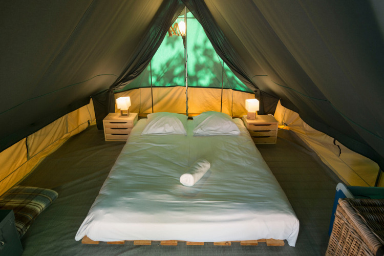Interieur van de Bonaventure tipi tent bij Huttopia la Clarée in Frankrijk met bed en lampen.