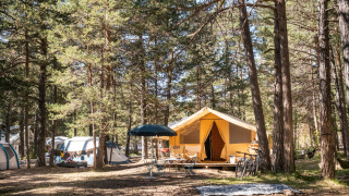 Safari tent Bungalow tent Classic in het bos, met fietsen, stoelen en andere tenten bij zonnig weer.