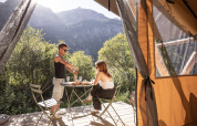 Coppia che si gode un pasto fuori dalla tenda safari Bungalow tent Classic a Huttopia la Clarée, in Francia, tra le montagne.