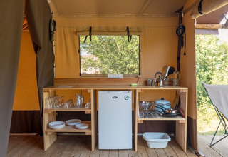 Petit coin cuisine dans une tente safari avec étagères en bois, vaisselle, réfrigérateur et ustensiles.