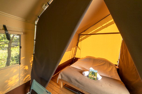 Intérieur d'une tente safari avec lit double, parquet en bois et fenêtre donnant sur la nature extérieure.