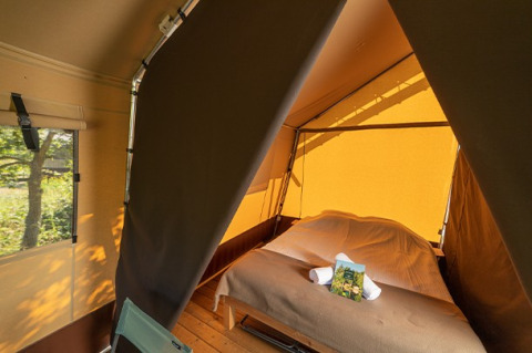 Innenansicht eines Safarizeltes mit einem Doppelbett, Holzfußboden und Ausblick ins Grüne durch das Fenster.