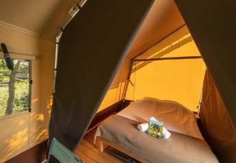 Interior of a safari tent with a double bed, wooden floor, warm lighting, and a window showing the outdoors.