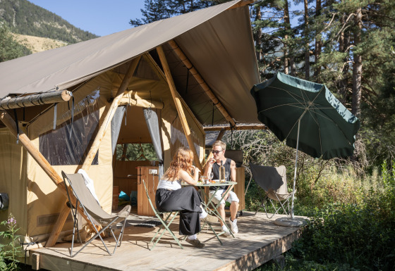 Due persone si rilassano davanti a una tenda safari Trappeur, immerse nella natura con ombrellone.