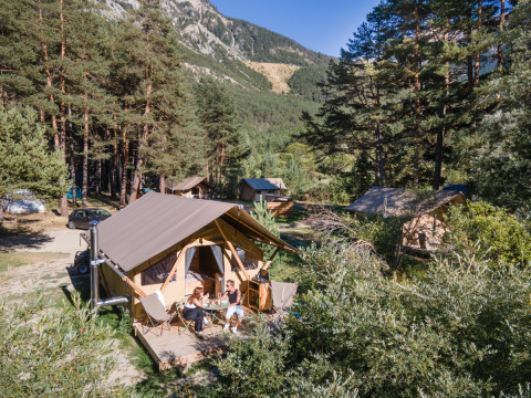 Tienda Trappeur tipo safari en Huttopia la Clarée, Francia, con personas relajándose rodeadas de árboles.