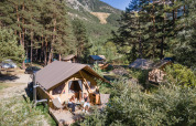 Tente safari Trappeur à Huttopia la Clarée, France, avec des personnes sur la terrasse au milieu des arbres.