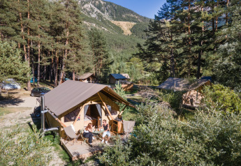 Trappeur safari tent at Huttopia la Clarée, France, with people relaxing on the deck surrounded by trees.