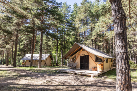 Tiendas safari Trappeur en Huttopia la Clarée, Francia, situadas en un claro de bosque soleado.