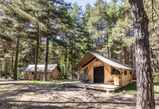 Tiendas safari Trappeur en Huttopia la Clarée, Francia, situadas en un claro de bosque soleado.